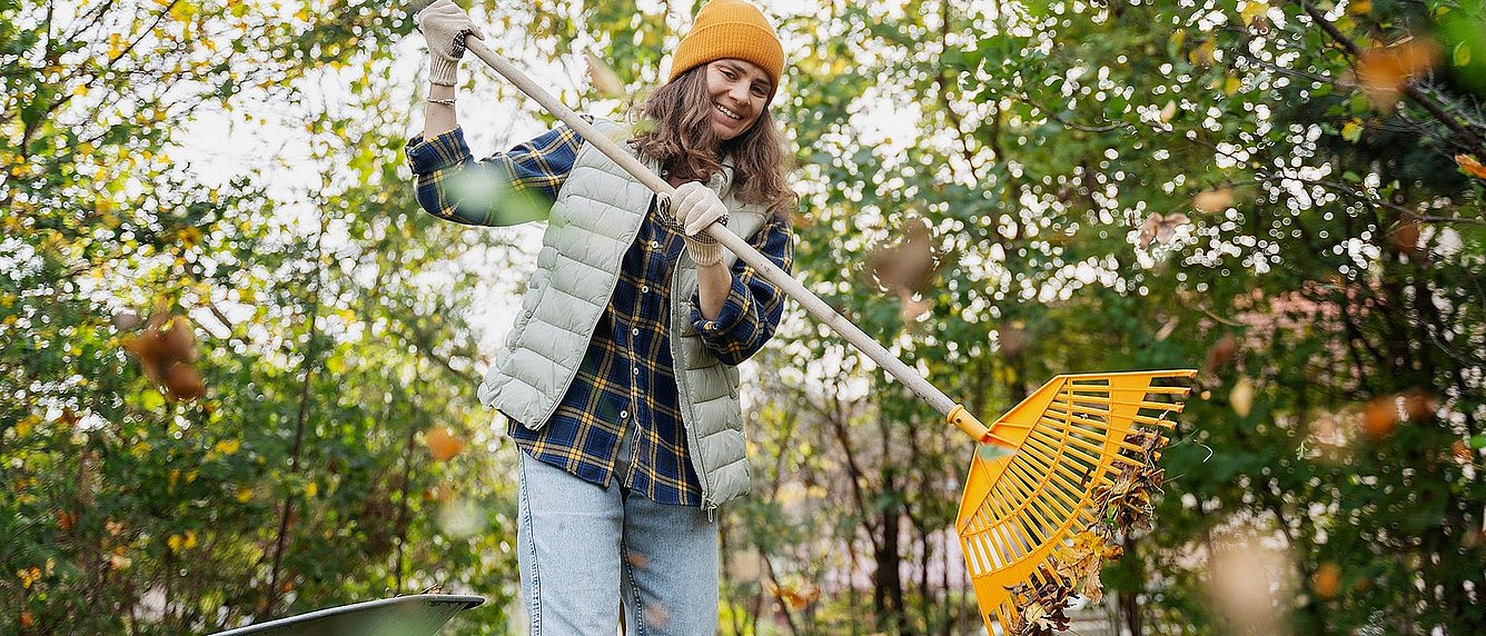 Frau sammelt im Herbst Laub im Garten